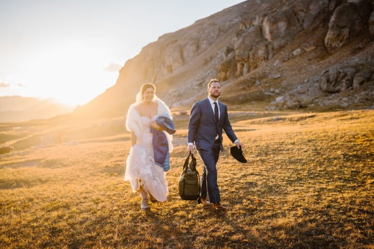 Couple hiking in the mountains with sun glaring behind them as they walk towards their elopement in Colorado.
